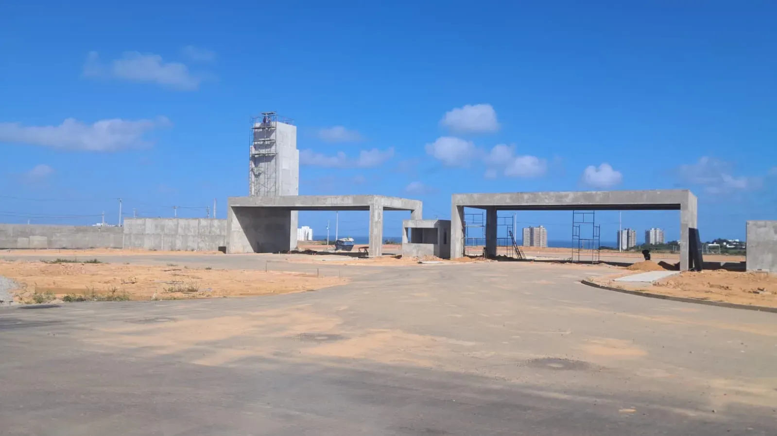 A portaria do Condomínio Tramonto com os dois pórticos de concreto, a torre do reservatório ao fundo e a calçada nova à direita
